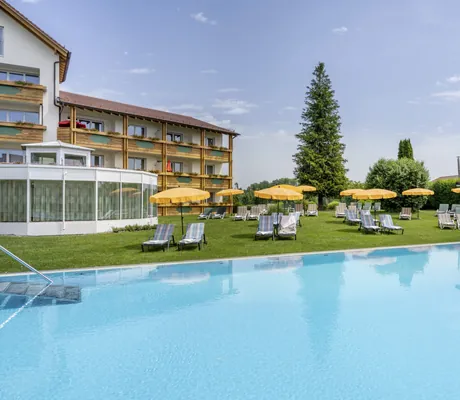 Outdoorpool mit orangen Sonnenschirmen in der Krone Schnetzenhausen mit Blick auf Zimmertrakt
