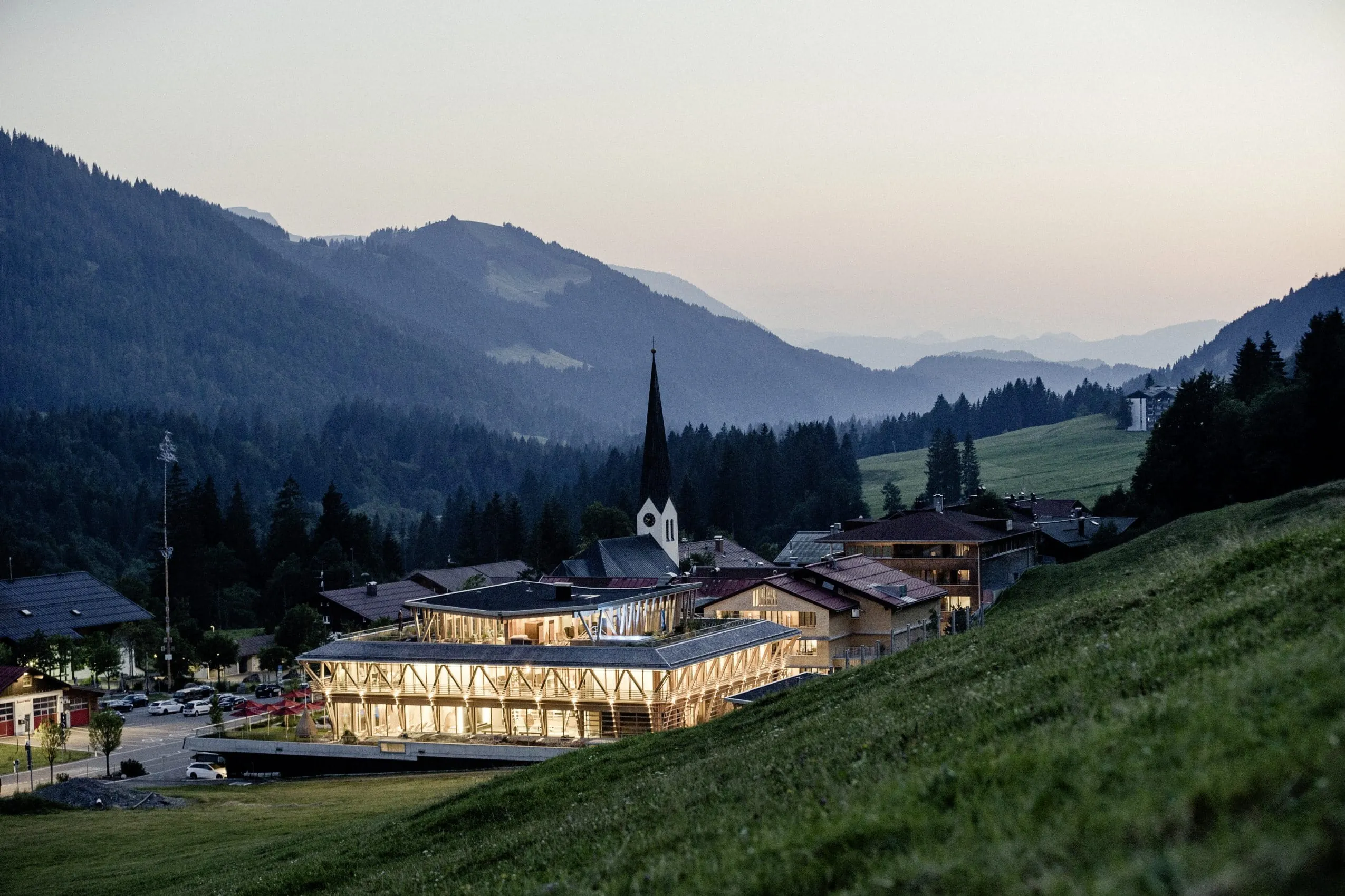 Blick aus der Luft auf das in der D&auml;mmerung beleuchtete HUBERTUS Mountain Refugio Allg&auml;u mit Bergpanorama im Hintergrund