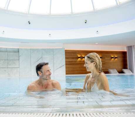 Paar sitzt lachend im Schwimmbecken mit Kuppel im Hotel Allgäu Sonne