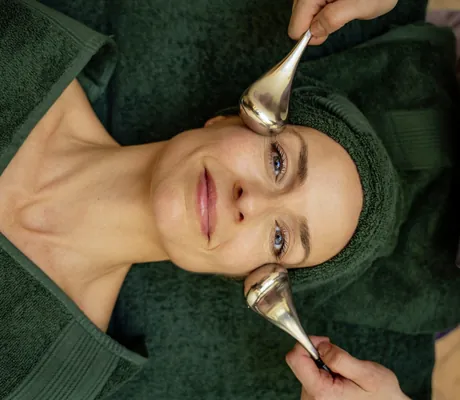 Frau mit dunkelgrünem Frotteeturban erhält im Hotel Allgäu Sonne Gesichtsbehandlung mit Icerollern