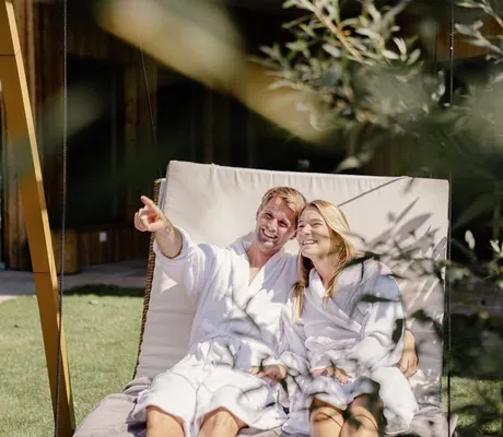 Paar in weißen Bademänteln liegt auf der Schaukelliege im Garten des Alpbacherhof