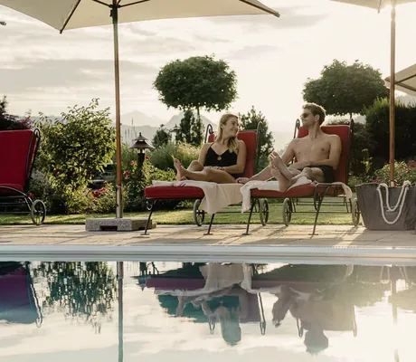 Paar liegt auf roten Liegestühlen am Outdoorpool im Alpbacherhof