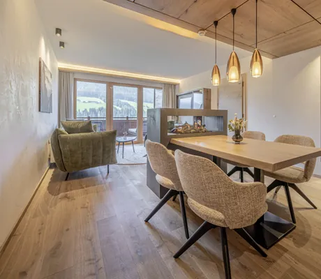 Tisch mit vier gepolsterten Sesseln unter drei Hängelampen in der Suite des Alpbacherhof