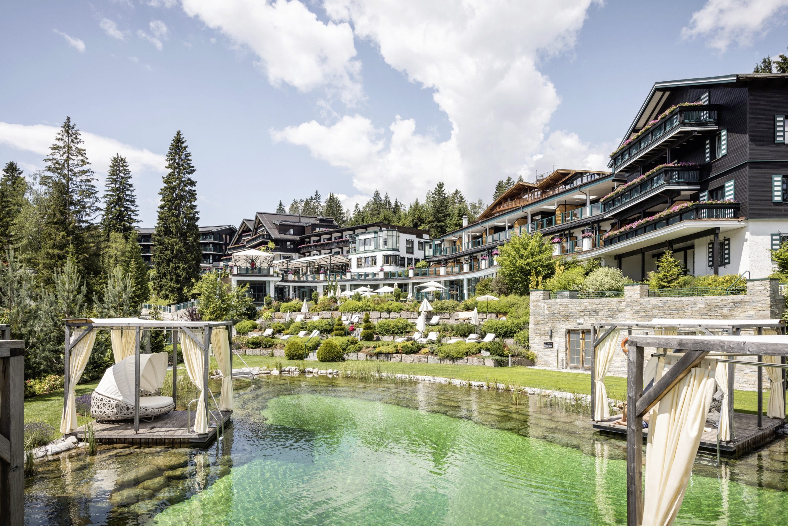 Fassade des Alpin Resort Sacher Seefeld mit Blick auf den Naturteich mit Holzinseln