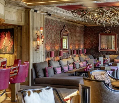 Blick von der Bar im Alpin Resort Sacher Seefeld mit roten Ledersesseln auf Loungeecke mit Geweihen an der Decke