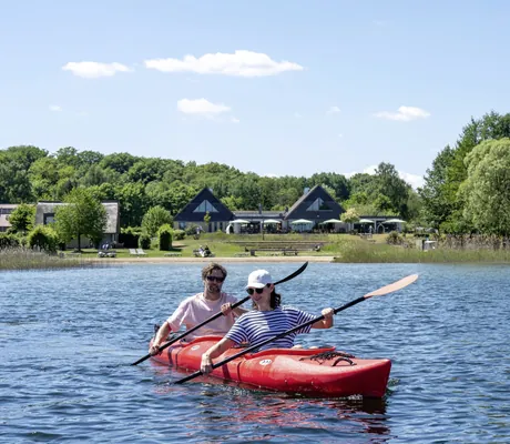 Paar paddelt in einem roten Kanu am Ufer des Plauer Sees entlang vor dem BEECH Resort Plauer See