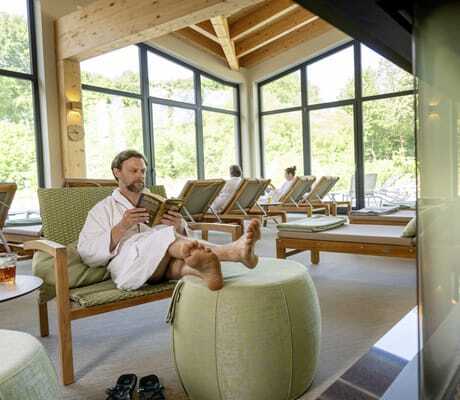 Mann liegt in weißem Bademantel auf grüner Liege am Kamin im Ruheraum des BEECH Resort Plauer See