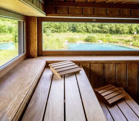 Blick von der Sauna im BEECH Resort Plauer See auf den türkisen Outdoorpool umgeben von Schilf