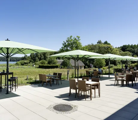 Terrasse im BEECH Resort Plauer See mit großen hellgrünen Sonnenschirmen und Blick auf den Strand und den See