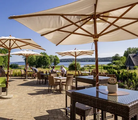 Terrasse im BEECH Resort Plauer See mit weißen Sonnenschirmen und Blick auf den See