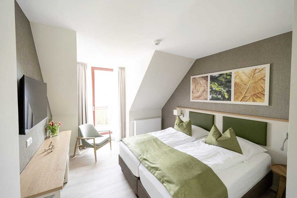 Zimmer im BEECH Resort Plauer See mit grünem Bettüberwurf und abgeschrägter Wand