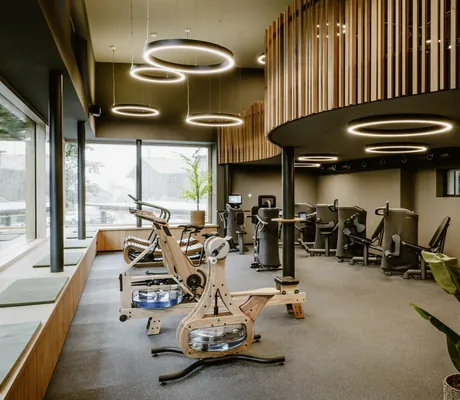 zweistöckiger Fitnessraum im Bergkristall Resort mit Noohrd-Geräten und runden Deckenleuchten