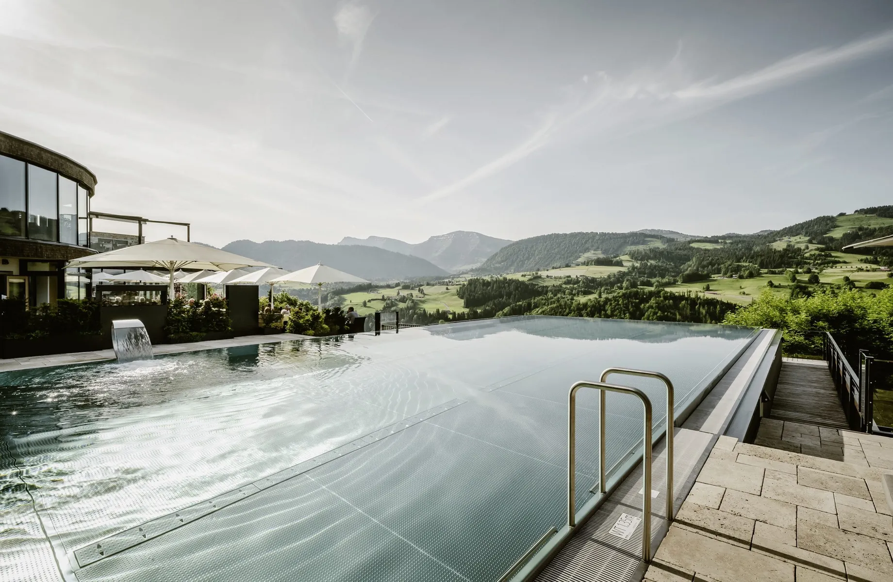 Infinity-Outdoorpool im Bergkristall Resort mit weißen Sonnenschirmen mit Blick auf den Hausberg