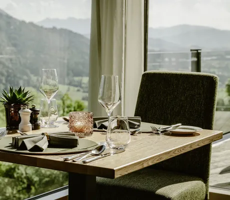 gedeckter Tisch im Restaurant des Bergkristall Resort mit moosgrünen Stühlen am Panoramafenster