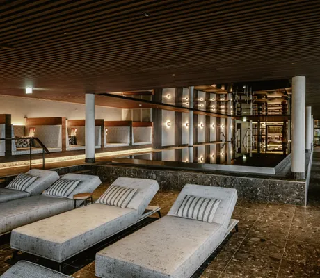 Indoorpool im Bergkristall Resort mit grauen Polsterliegen und marmoriertem Boden