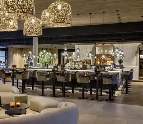 Blick von der Lobby auf die Bar im Das Mühlbach mit grauen Sitzgruppen mit Hochstühlen