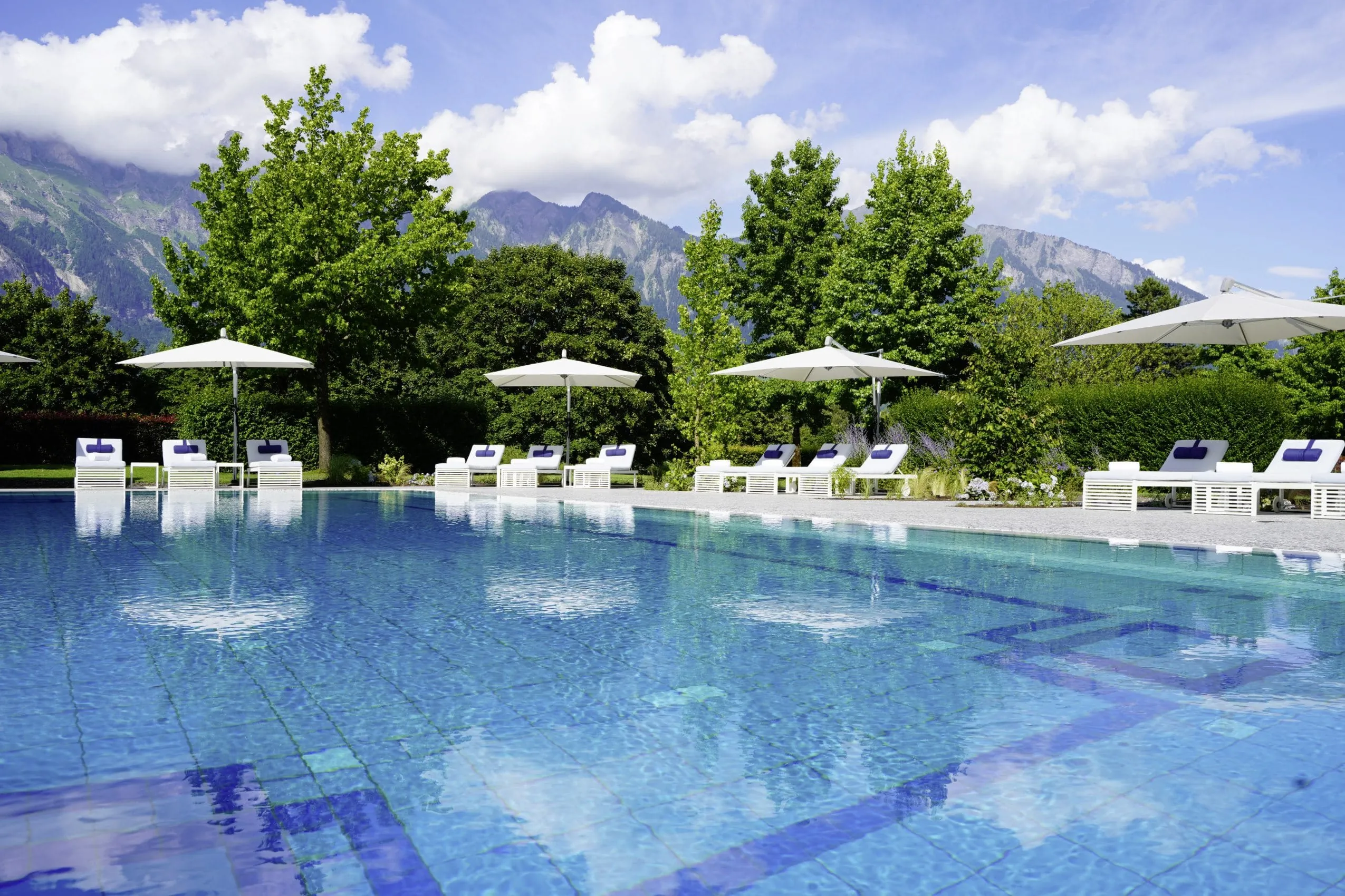 Outdoorpool im Grand Resort Bad Ragaz mit weißen Liegen und Sonnenschirmen mit Blick auf die Berge