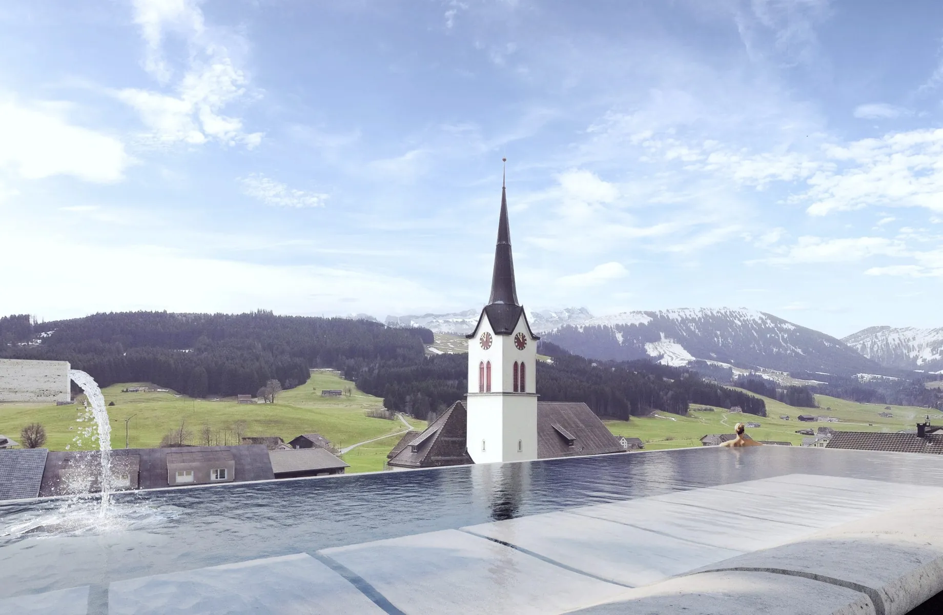 Infinitypool auf dem dach des Huus Quell mit Blick auf den Kirchturm und die Berge