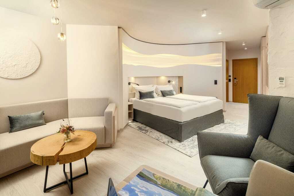 Suite im Kurhotel an der Obermaintherme mit taupefarbenem Bett in einer Nische und Tisch aus einer Baumscheibe