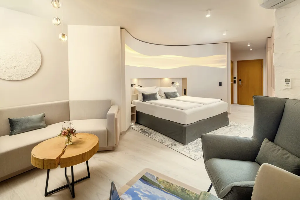 Suite im Kurhotel an der Obermaintherme mit taupefarbenem Bett in einer Nische und Tisch aus einer Baumscheibe