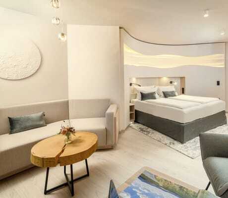 Suite im Kurhotel an der Obermaintherme mit taupefarbenem Bett in einer Nische und Tisch aus einer Baumscheibe