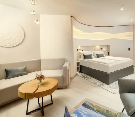 Suite im Kurhotel an der Obermaintherme mit taupefarbenem Bett in einer Nische und Tisch aus einer Baumscheibe