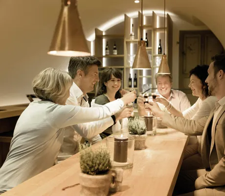 Gruppe von menschen sitzt an einem langen Holztisch in der Kuroase im Kloster und prostet sich zu