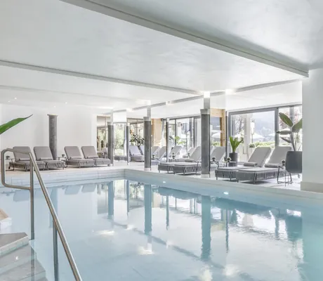 Indoorpool im Lärchenhof mit geflochtenen Ruheliegen und großen Pflanztöpfen