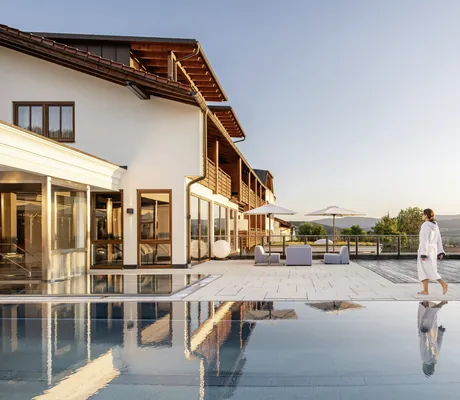Frau in weißem Bademantel läuft am Outdoorpool des Landromantikhotel Oswald entlang