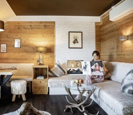 dunkelhaarige Frau sitzt in gemütlicher Sofaecke mit Holzwänden in Landromantikhotel Oswald und liest ein Buch