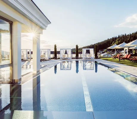 Outdoorpool im Landromantikhotel Oswald mit weißen Daybeds und roten gepolsterten Liegen