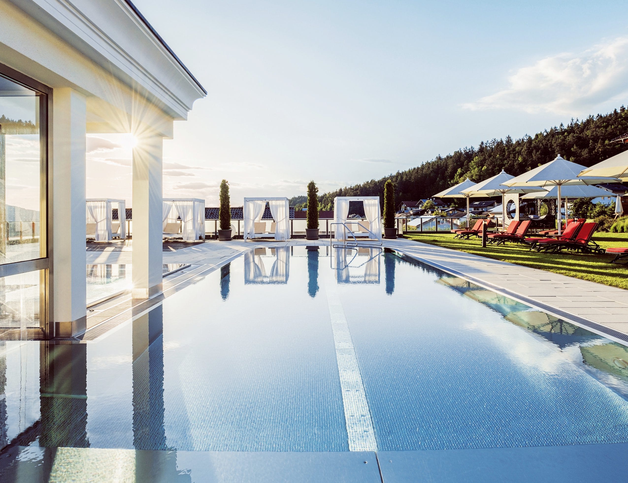 Outdoorpool im Landromantikhotel Oswald mit weißen Daybeds und roten gepolsterten Liegen