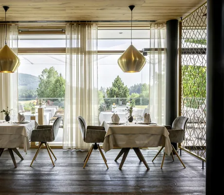 eingedeckte Tische im Restaurant des Mooshof mit großen goldenen Hängeleuchten mit Blick auf die Terrasse
