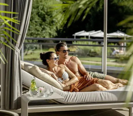Paar mit Sonnenbrillen liegt in Daybed am Pool des Mooshof