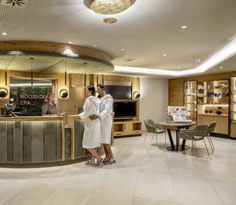 Paar in weißen Bademänteln steht an der Spa-Rezeption des Mooshof und lässt sich beraten