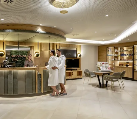 Paar in weißen Bademänteln steht an der Spa-Rezeption des Mooshof und lässt sich beraten