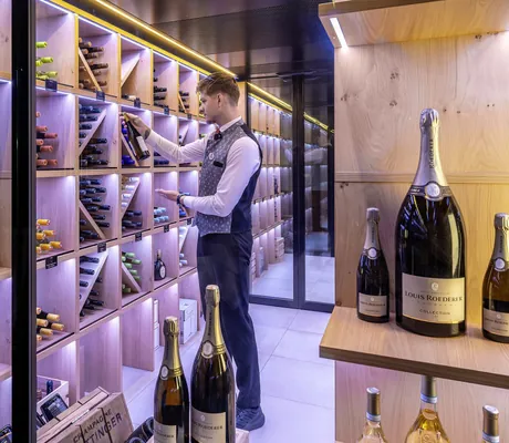 Mann in Weste prüft eine Weinflasche in der Vinothek des Mooshof