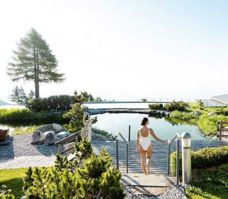 Frau in weißem Badeanzug geht dir Treppe hinunter zum Teich und zum Pool im Mountain Resort Feuerberg
