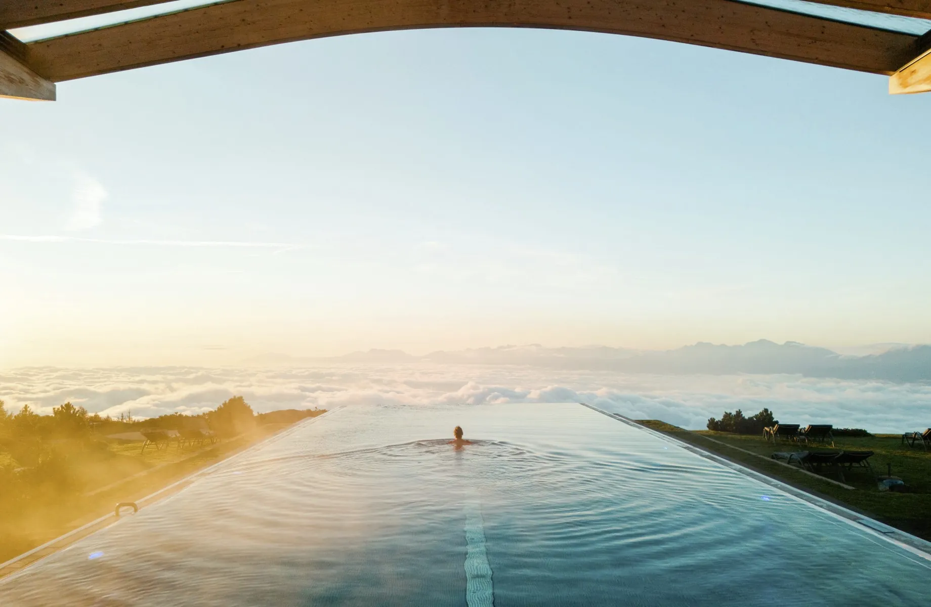 Frau schwimmt im Infinitypool des Mountain Resort Feuerberg in Richtung Abendsonne