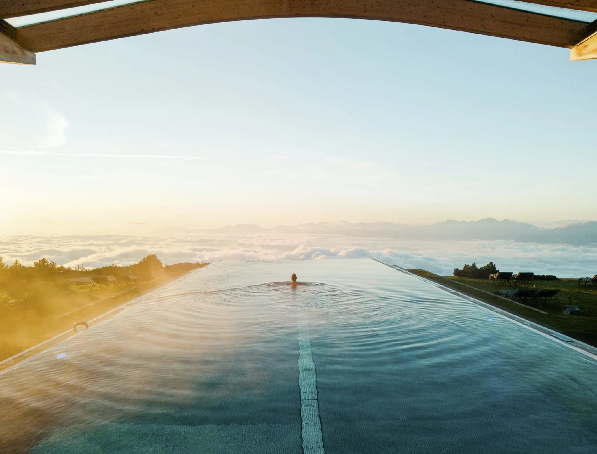 Frau schwimmt im Infinitypool des Mountain Resort Feuerberg in Richtung Abendsonne