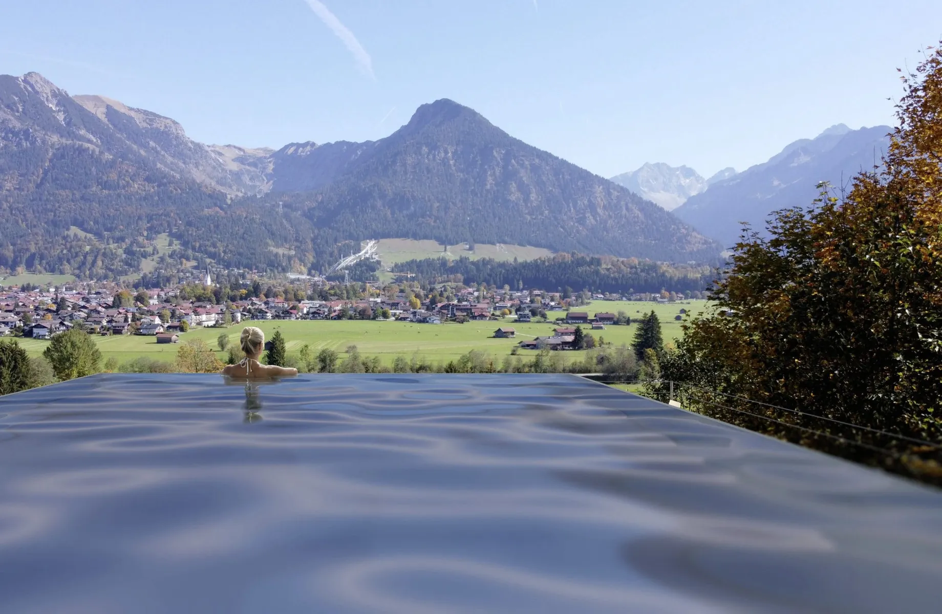 Frau steht am and des Infinitypools des Naturhotel Waldesruhe und schaut in die Berge