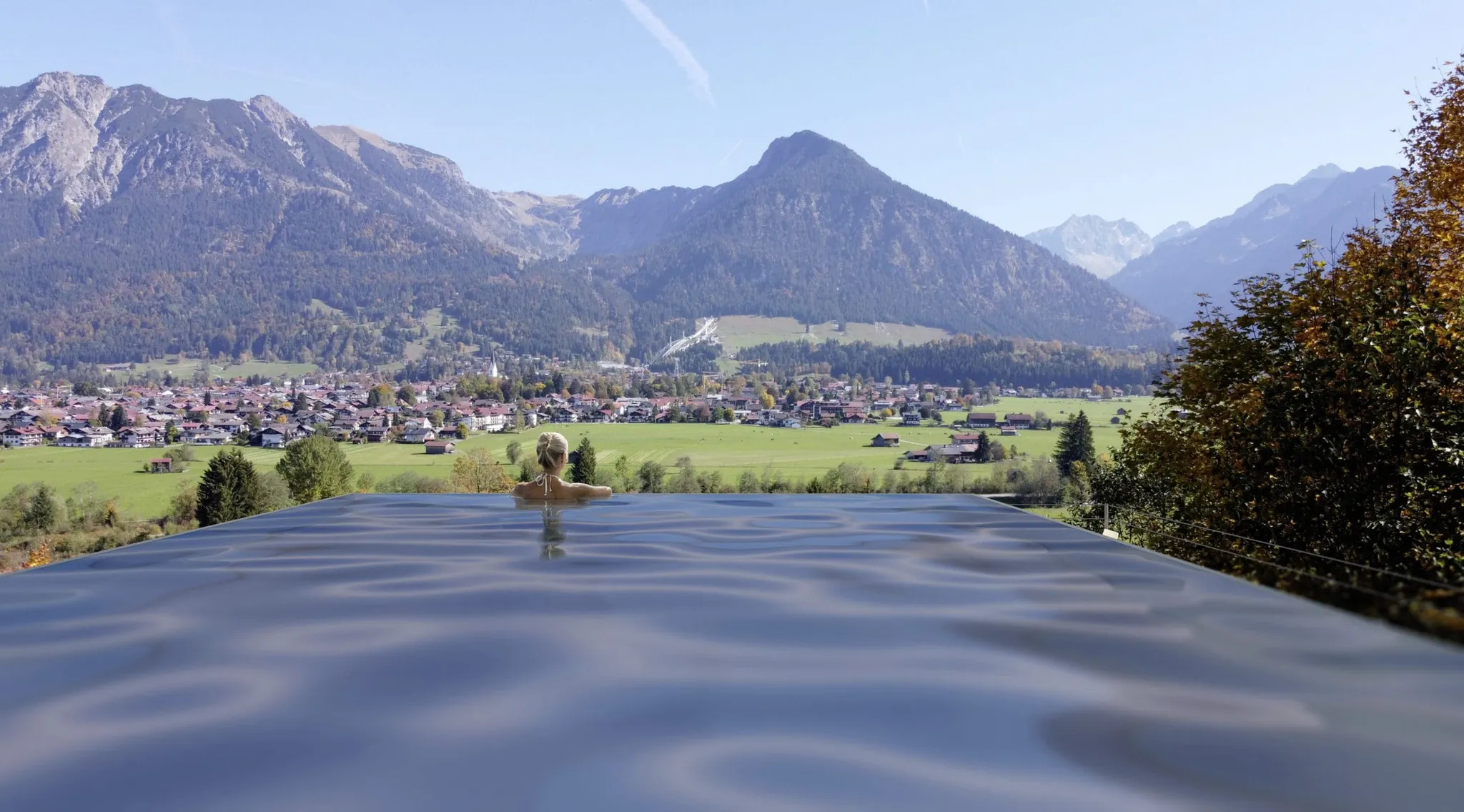 Frau steht am and des Infinitypools des Naturhotel Waldesruhe und schaut in die Berge