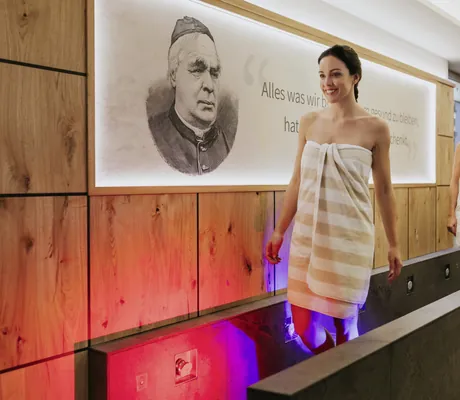 zwei Frauen mit gelb-weiß gestrieften Handtüchern laufen im Ortner's Resort im Kneippbecken