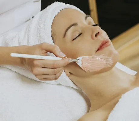 Frau mit weißem Frotteturban erhält rosafarbene Maske im Ortner's Resort