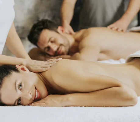 Paar wird im Ortner's Resort von zwei Therapeuten massiert und Frau lächelt in die Kamera