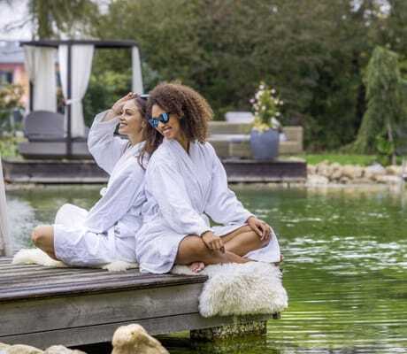zwei Frauen mit Sonnenbrillen und im Bademantel sitzen im Schneidersitz am Badeteich im Ortner's Resort