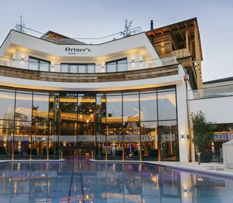 Panoramafenster vom Outdoorpool mit Blick in den Wellnessbereich des Ortner's Resort am Abend