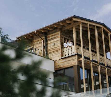 Paar in weißen Bademänteln steht auf Balkon des Holzzubaus des Ortner's Resort