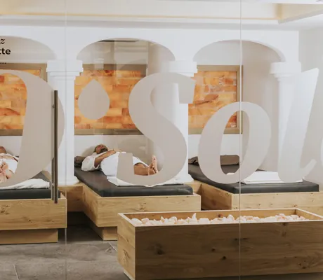 zwei Personen liegen auf braunen Liegen im Salzraum mit Salzwand des Ortner's Resort