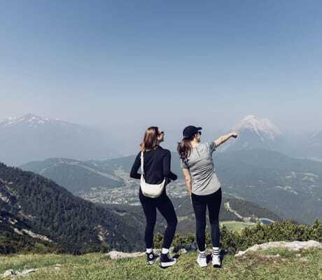 zwei Frauen in schwarzer leggings stehen auf dem Berg und schauen auf die Gipfel in der Ferne